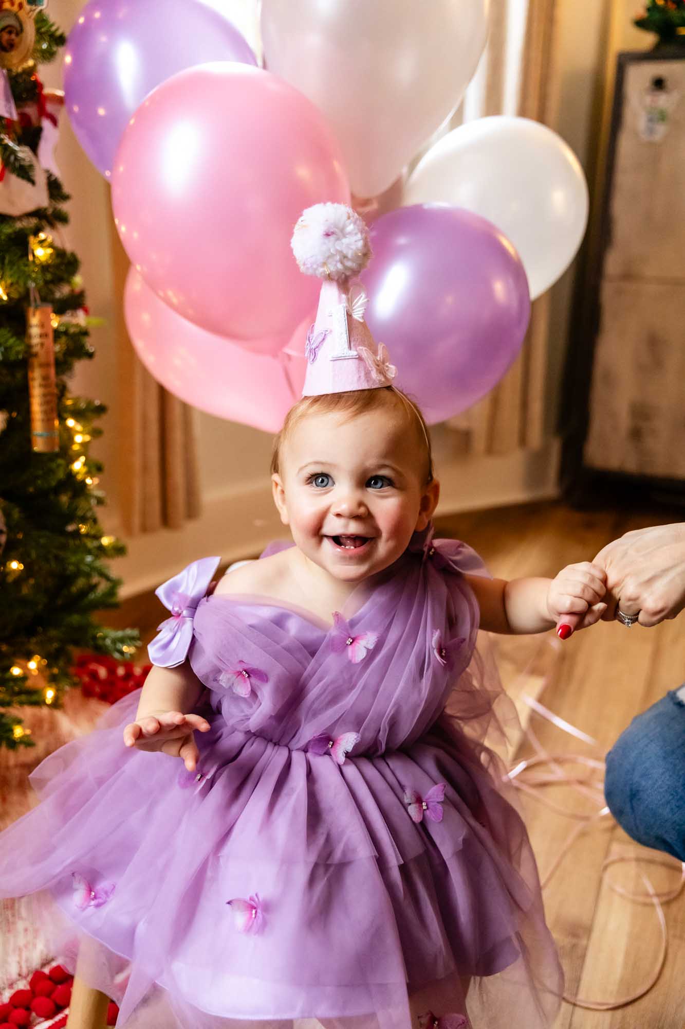 little girl in purple dress and birthday hat, standing in front of balloons